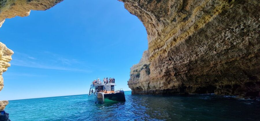 A catamaran anchored off a limestone headland with swimmers in the water